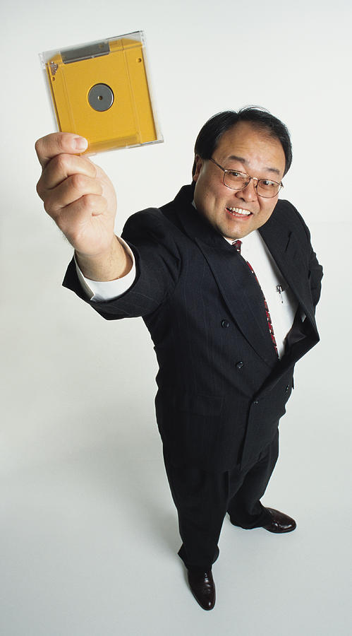 A Handsome Middle Aged Asian Businees Man With Glasses Dressed In A Business Suit Looking Up Into The Camera Holiding Up A Yellow Zip Disk Photograph by Photodisc