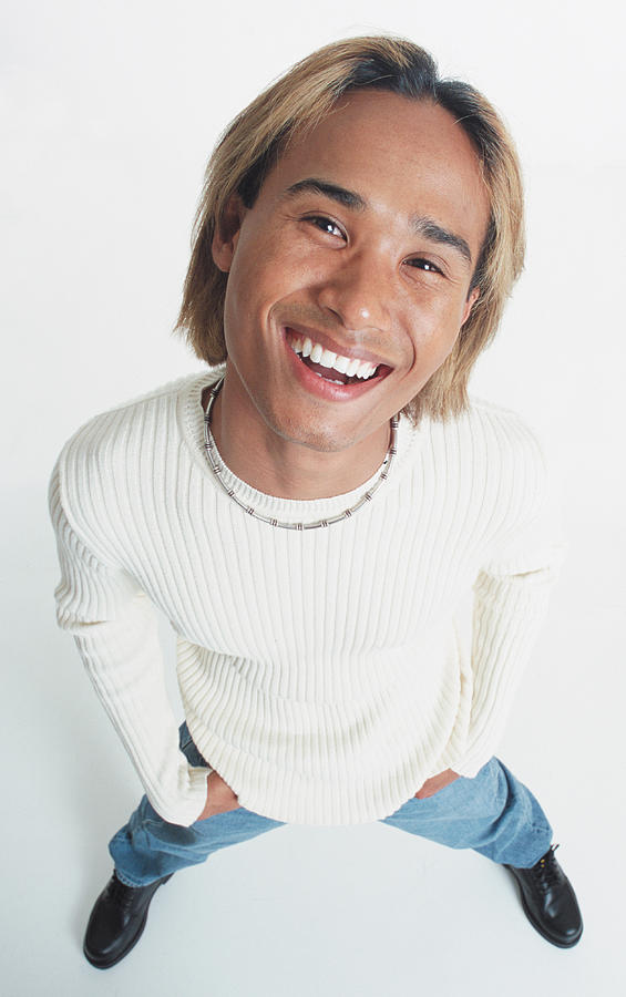 A Handsome Young Asian Man With Bleached Hair Stands Looking Up At The Camera Wearing A White Long Sleeve Shirt And A Shell Necklace Photograph by Photodisc
