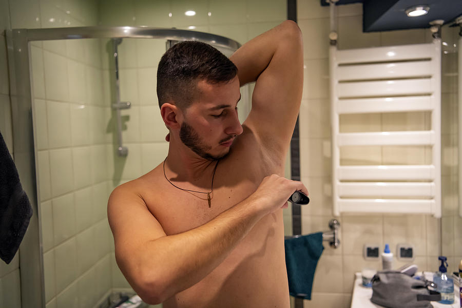 A Handsome Young man is Using Deodorant in the Bathroom Photograph by RealPeopleGroup