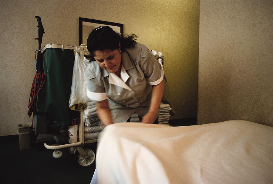 A Hispanic Woman At A Hotel Room Tucks Bedsheets Into A Bed Photograph by Photodisc