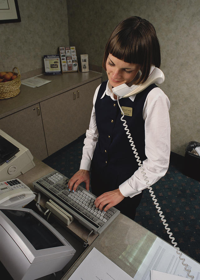 A Hotel Attendant Logs A Customer Reservation Onto A Computer While Speaking With Him Over The Telephone Photograph by Photodisc
