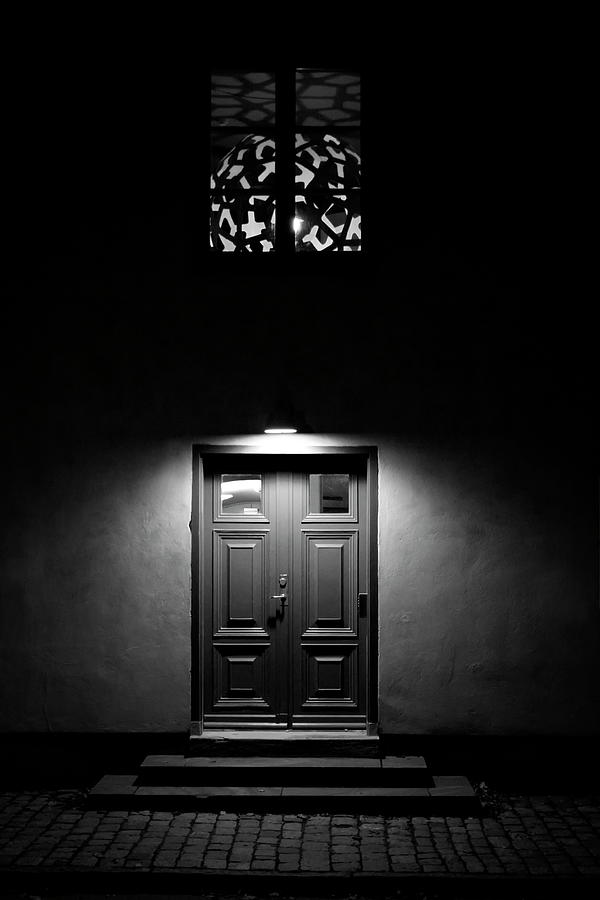 A light cone is illuminating the wooden door to a town house in a dark night - monochrome Photograph by Ulrich Kunst And Bettina Scheidulin