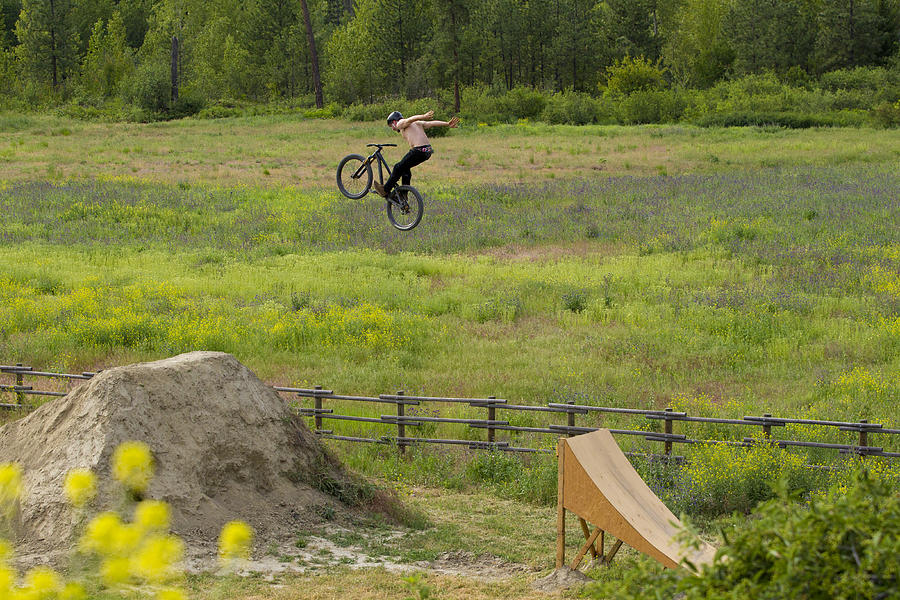 A male mountain bike rider does a no hander trick off a big jump in the summertime. Photograph by GibsonPictures