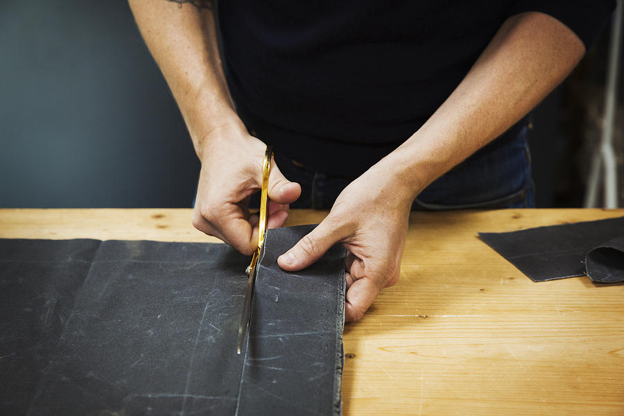 A man cutting a piece of grey fabric with shears. Photograph by Mint Images
