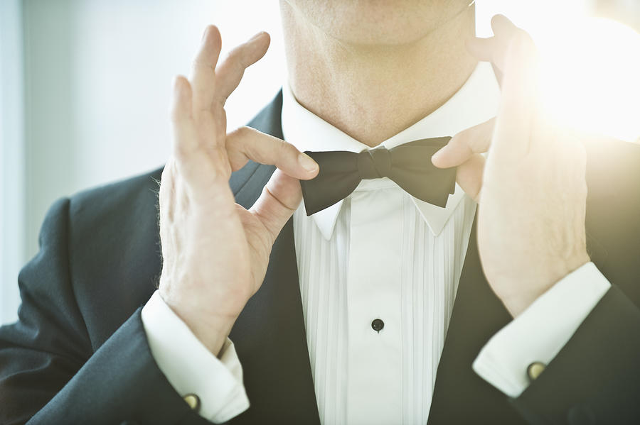 A man in a tuxedo fixing his bowtie Photograph by Tetra Images - Daniel Grill