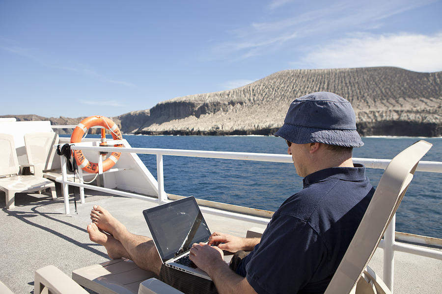 A man on his laptop on the deck of a boat Photograph by Noel Hendrickson