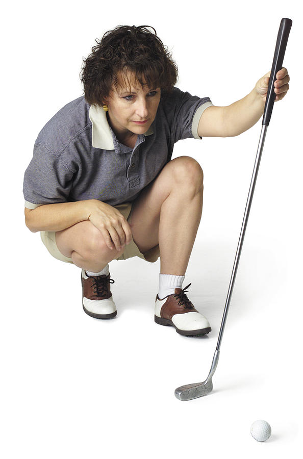 A Middle Age Caucasian Female Golfer In A Stripped Shirt Crouches Down With Her Putter And Lines Up A Shot Photograph by Photodisc