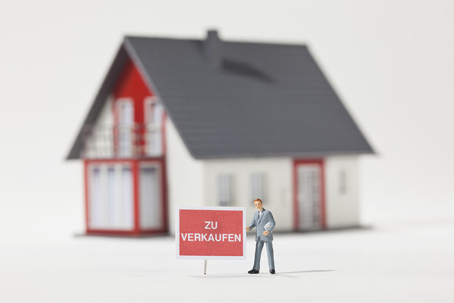 A miniature real estate agent figurine next to a ZU VERKAUFEN (for sale in German) sign Photograph by Caspar Benson