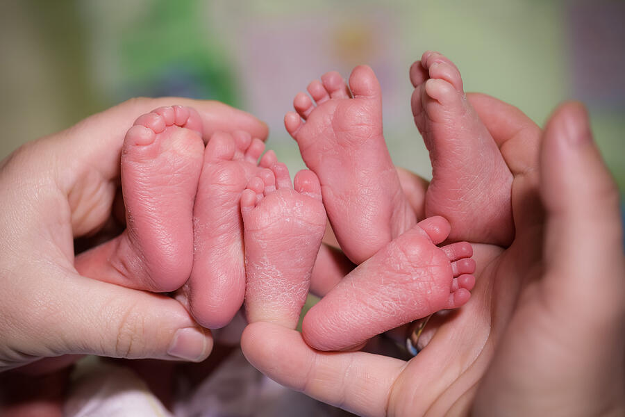 A mother is holding in the hands feet of newborn triplets baby. Photograph by Pirotehnik