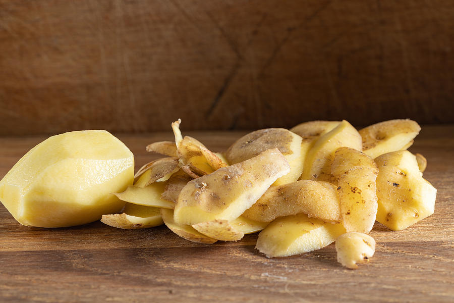 A peeled potato and pile of potatoes peel or skin on wood Photograph by Sebastian Radu