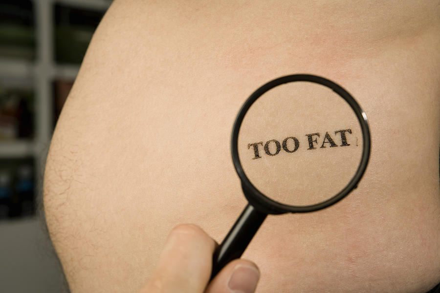 A person holding a magnifying glass to a mans abdomen stamped Too Fat Photograph by Martin Diebel