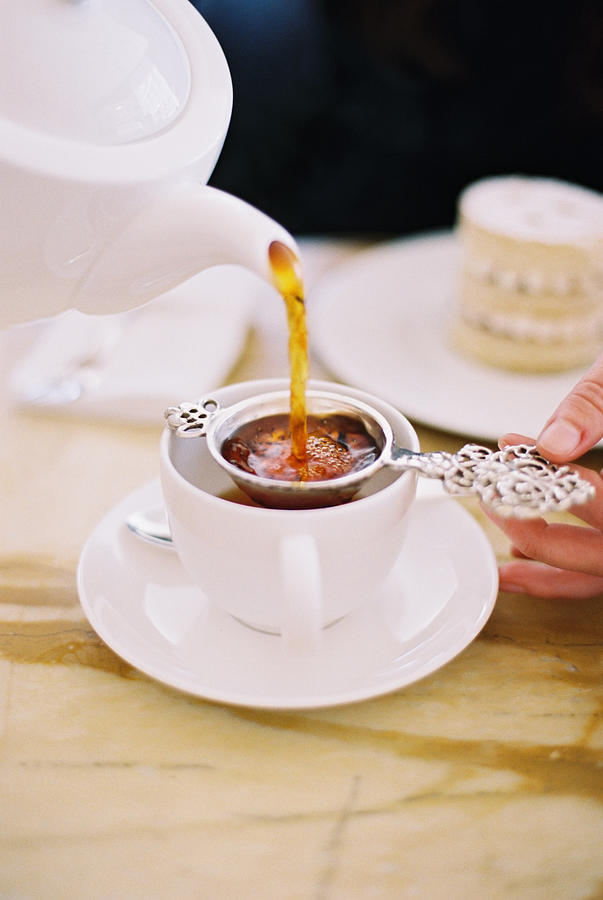 A person pouring a cup of tea, using a strainer. White china. Elegant afternoon tea. Photograph by Mint Images - Britt Chudleigh