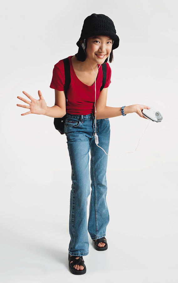 A Pretty Asian Preteen Girl Wearing A Red Teeshirt And Blue Jeans Has On A Black Hat And Is Leaning Towards The Camera As She Wears A Backpack And Spreads Her Arms While Listening To A Walkman Stereo Photograph by Photodisc