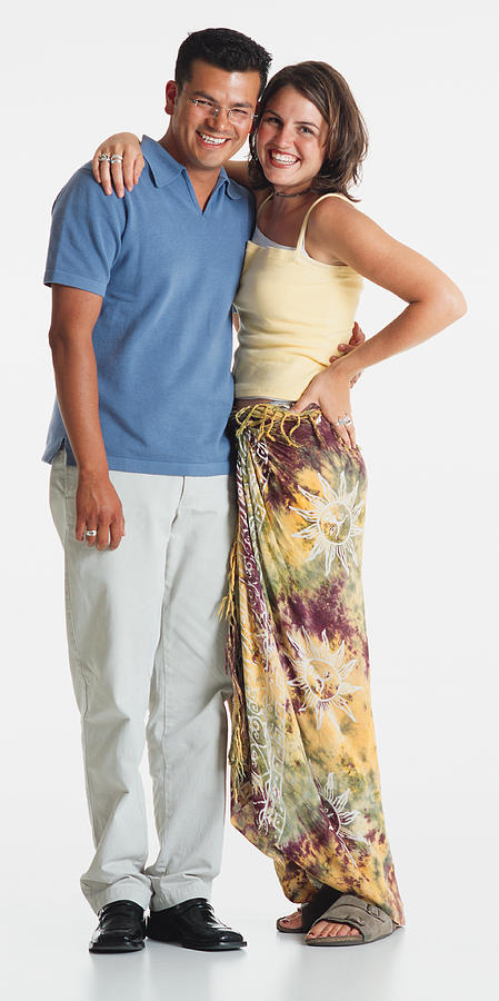 A Pretty Young Caucasian Woman In A Tank Top And Tye Dyed Skirt Stands With Her Arm Around A Handsome Young Latino Man In White Slacks And A Blue Polo Shirt Photograph by Photodisc
