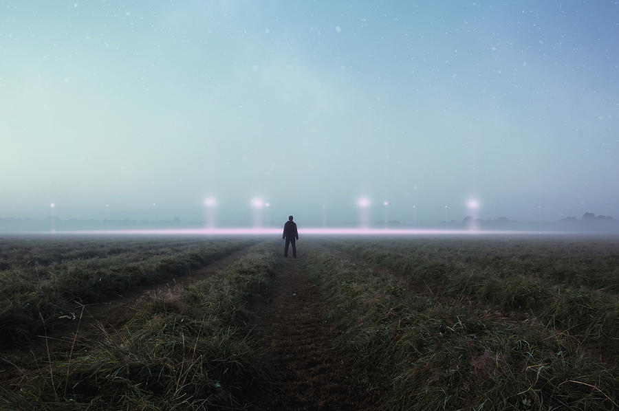 A science fiction concept. A man standing in a field back to camera looking into the sky, with glowing UFO orbs on the horizon Photograph by David Wall