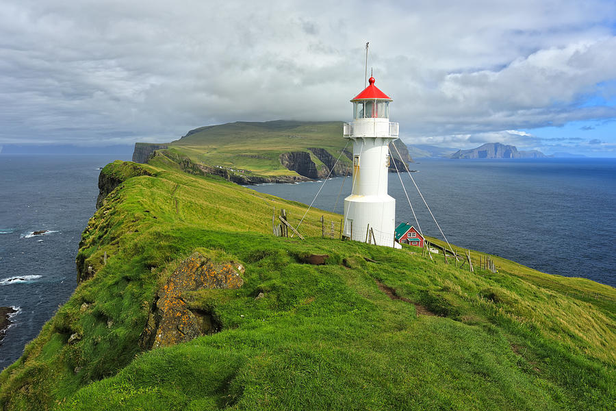 A small white lighthouse wit a red roof on top of grassy cliffs of Mykines Island Photograph by Rainer Grosskopf