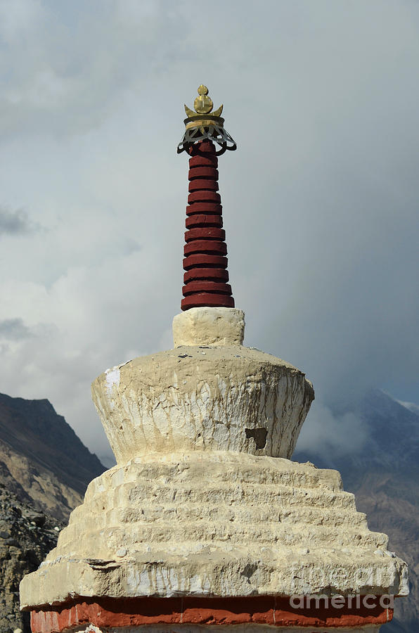 A stupa with a stone base and red spire with mountains in the ...