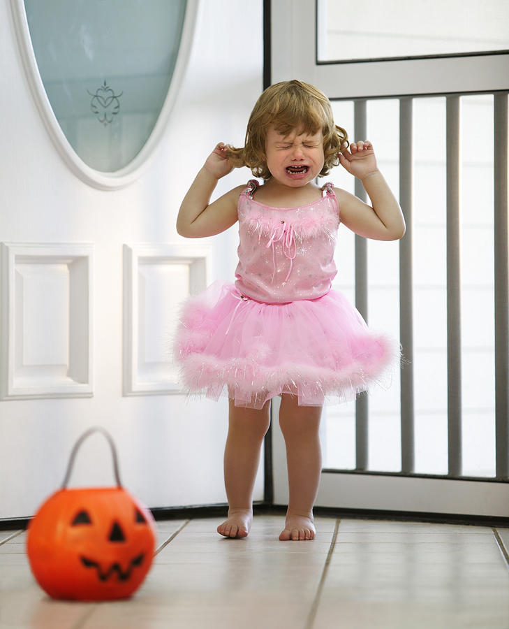 A toddler dressed in a ballet outfit for Halloween chooses candy from her pumpkin bucket Photograph by Thinkstock