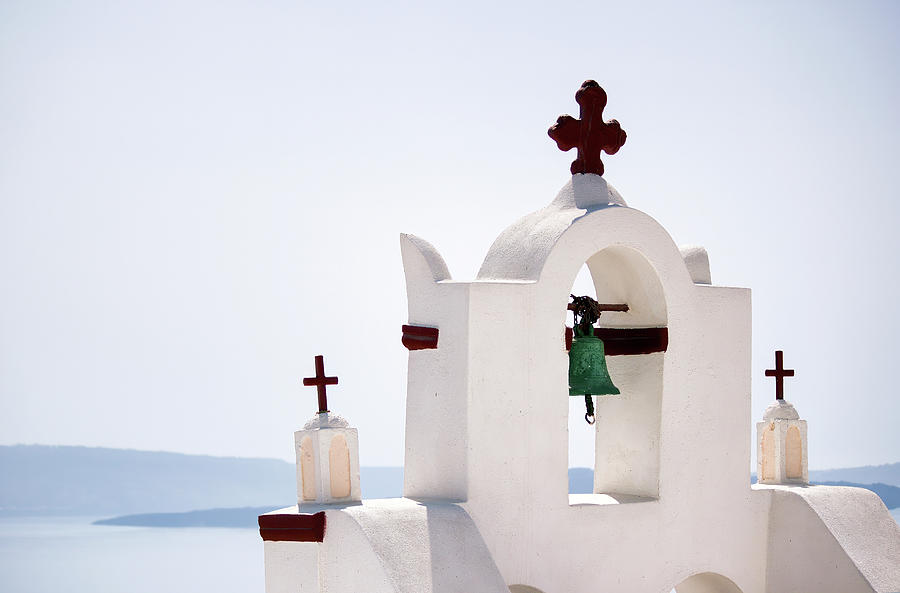 A tower top of a church with cross sign and bells architecture located in oia village in one of Cycladic island in Santorini, Greece against sea. Photograph by Arpan Bhatia