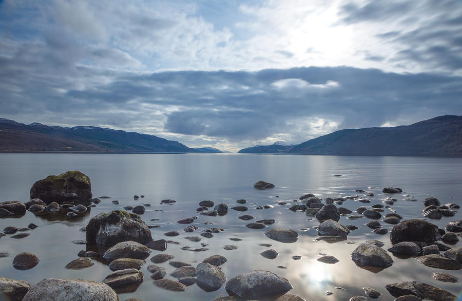 A view across Loch Ness looking down the length of the lake with rocks inn the foreground and dark clouds above, in Scotland Photograph by Luke Richardson