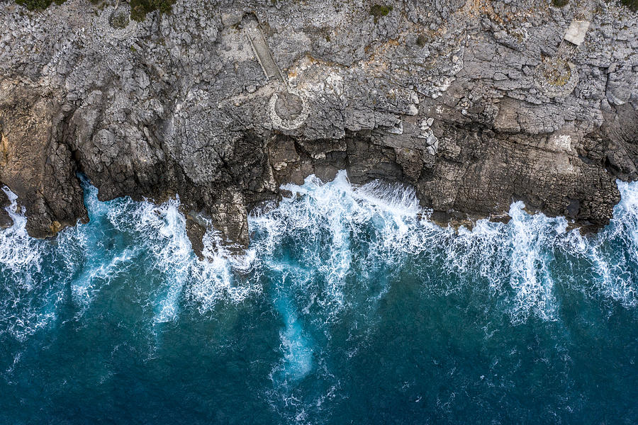 A view directly above a steep rocky shoreline coming out of the sea Photograph by Extreme Media