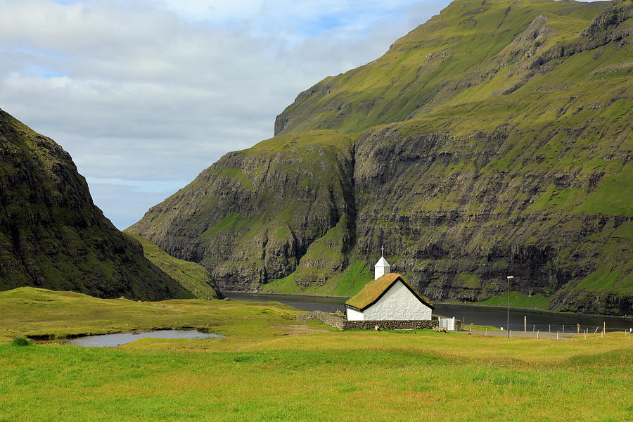 A white stone church with a grassy roof above a bay between high mountains Photograph by Rainer Grosskopf