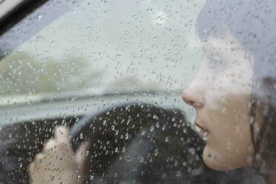 A woman driver sitting in car looking out window, raindrops on window Photograph by fStop Images - Vladimir Godnik