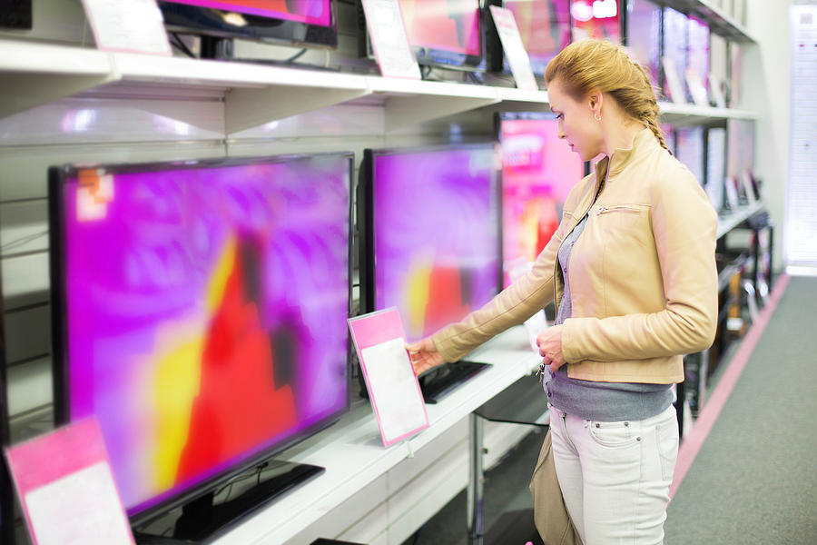 A woman observing prices for a television in a store Photograph by 97