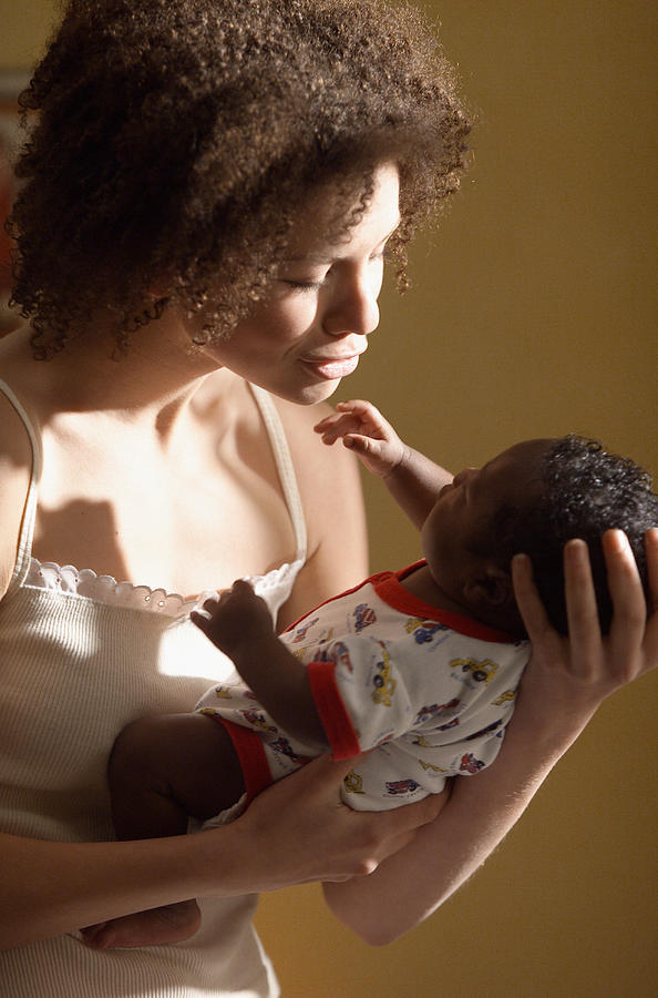 A Young African American Mother Holds Her Newborn Son Close As She Examines Him Lovingly Photograph by Photodisc
