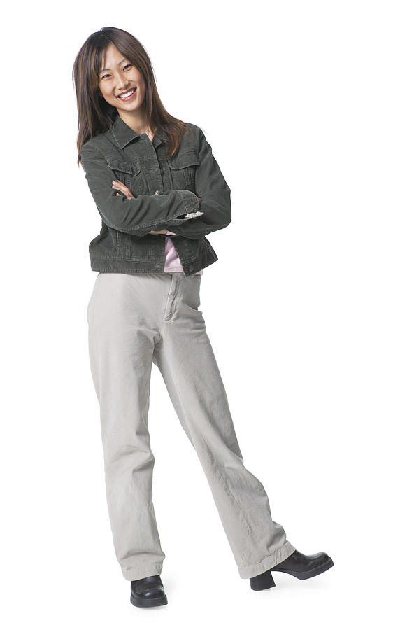 A Young Asian Woman Dressed In Tan Pants And A Jean Jacket Folds Her Arms Leans To One Side And Smiles Photograph by Photodisc