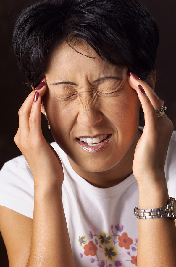 A Young Asian Woman With Short Hair Holds Her Fingers To Her Temples And Squints Her Eyes Shut As If In Pain Photograph by Photodisc