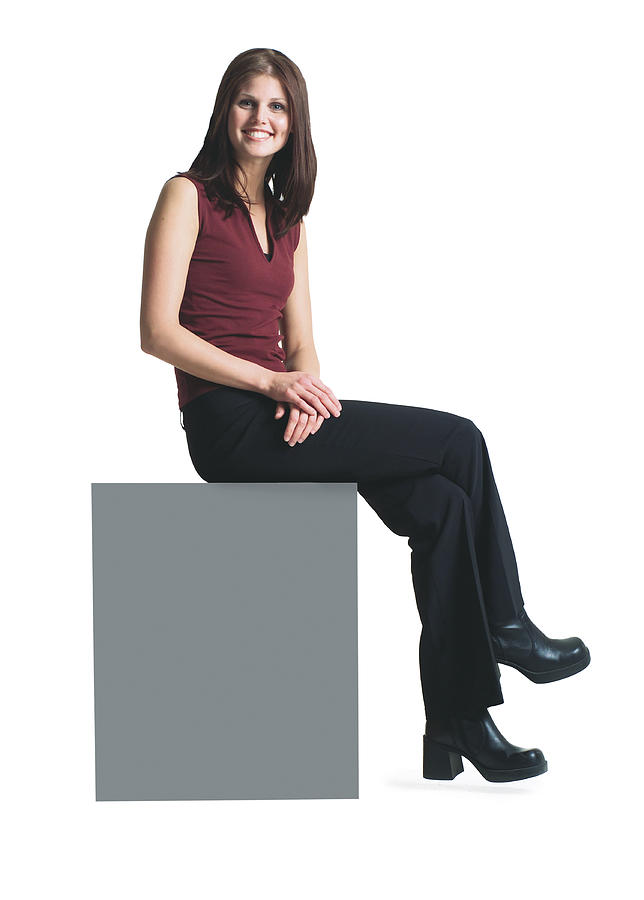 A Young Attractive Caucasian Woman In Black Pants And A Red Shirt Sits Atop A Blank Sign Smiling Photograph by Photodisc