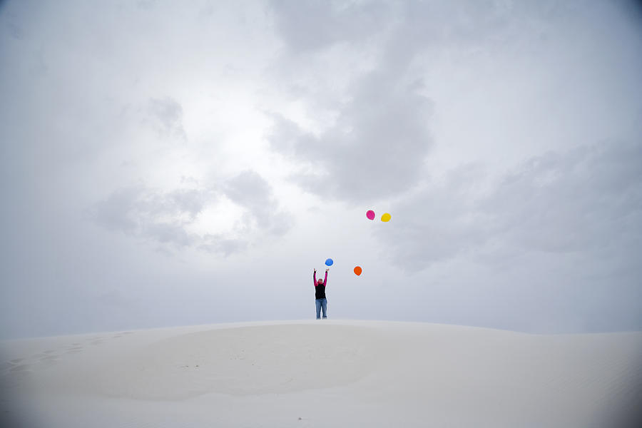 A young girl letting balloons go on a sand-dune. Photograph by Adam Hester
