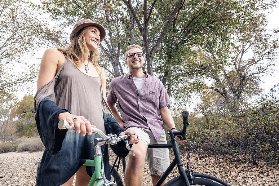 A young, happy man and woman smiling with bicycles in a park for fitness Photograph by Robb Reece