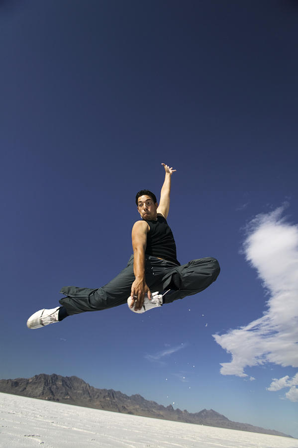 A Young Hispanic Man Jumps Playfully Through The Air In The Wide Open Space Of A Desert Photograph by Photodisc