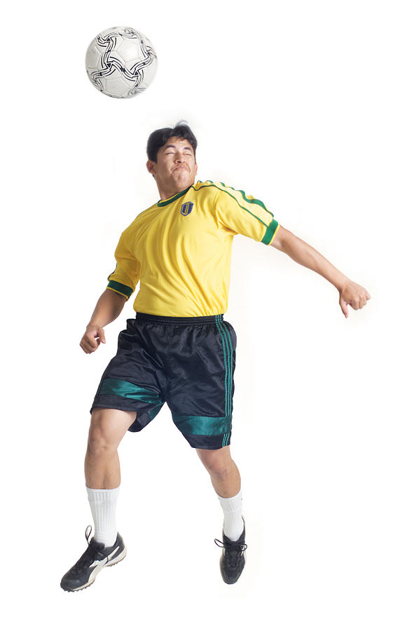 A Young Latin Male Wearing A Yellow Jersey Jumps And Hits A Soccer Ball With His Head Photograph by Photodisc