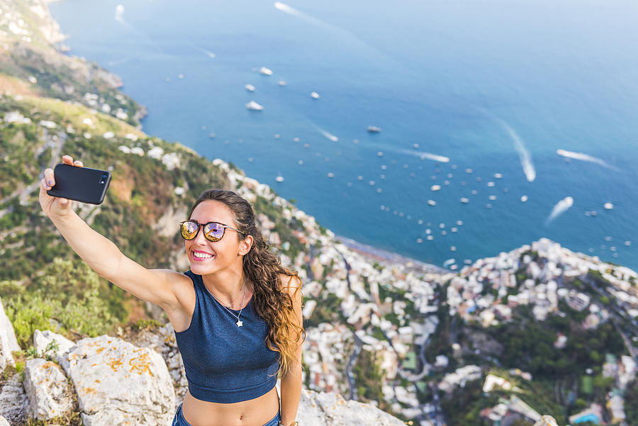 A young woman is taking a selfie. Positano village in the background Photograph by Andrea Comi