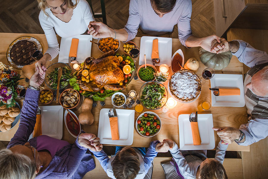 Above view of extended family saying grace before Thanksgiving dinner. Photograph by Skynesher