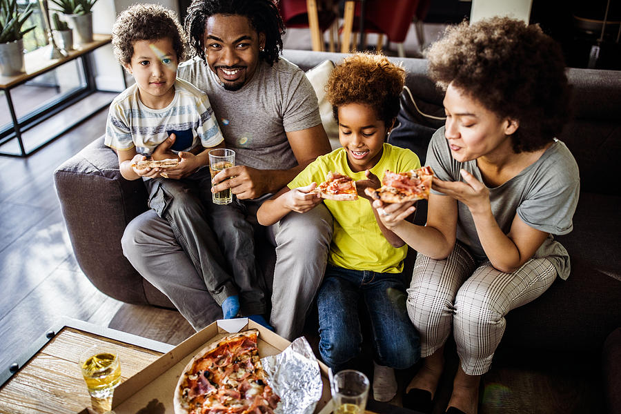 Above view of happy black family eating pizza at home. Photograph by Skynesher