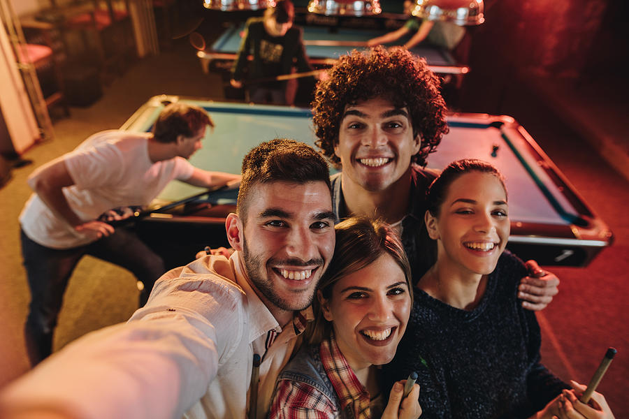 Above view of happy friends taking a self portrait photography in a pool hall. Photograph by Skynesher