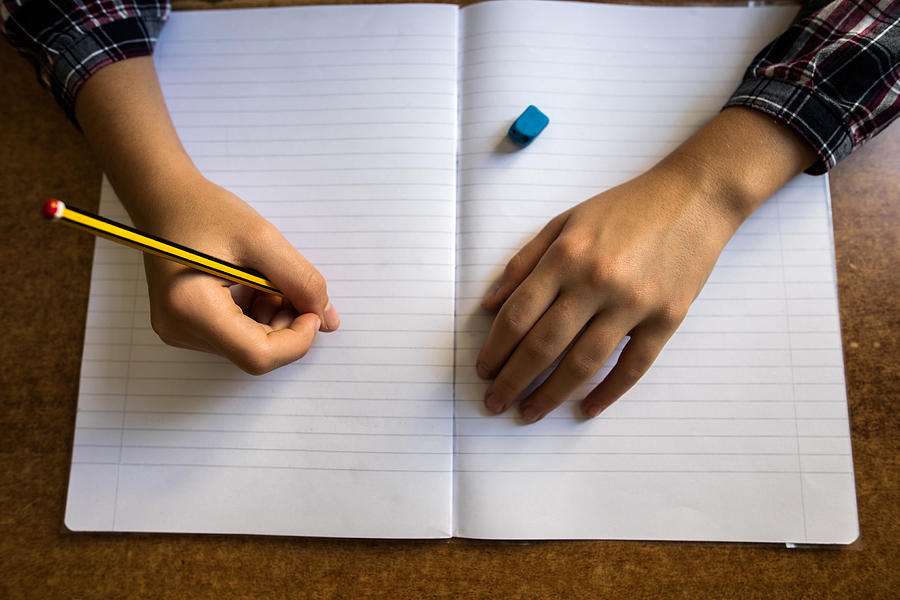 Above view of unrecognizable child writing into notepad. Photograph by Skynesher