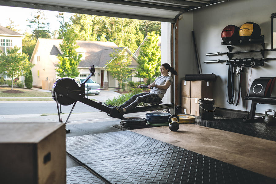 Active woman exercising on a rowing machine in her home garage gym during covid-19 pandemic. Photograph by IngredientsPhoto
