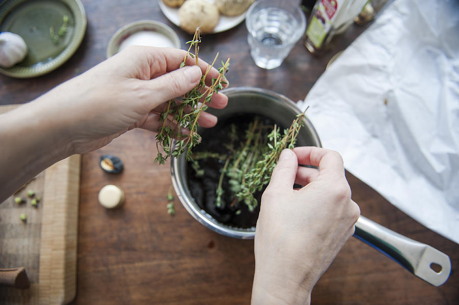 Adding thyme to a cooking pot Photograph by Lucy Lambriex