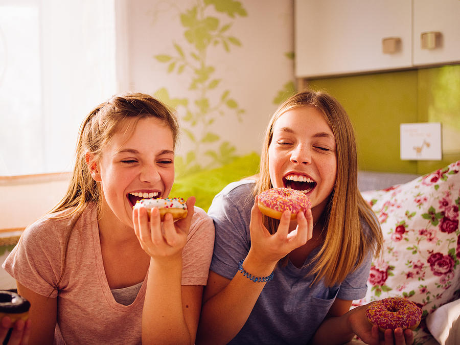 Adolescent girls eating coulourful doughnuts in a bright bedroom Photograph by Wundervisuals
