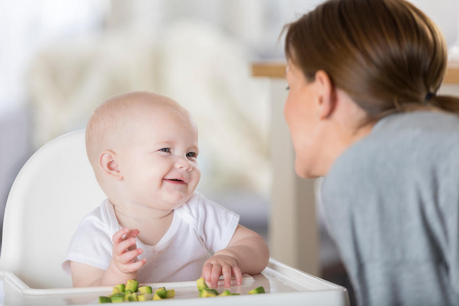 Adorable baby laughs at mom while eating finger food Photograph by SDI Productions
