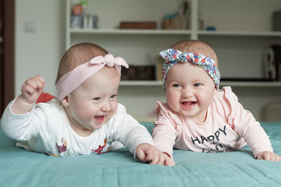 Portrait Photograph - Adorable baby twins having fun in bed at home. Cute kids with hairbands, ribbons, smiling, laughing. by Michael Dechev