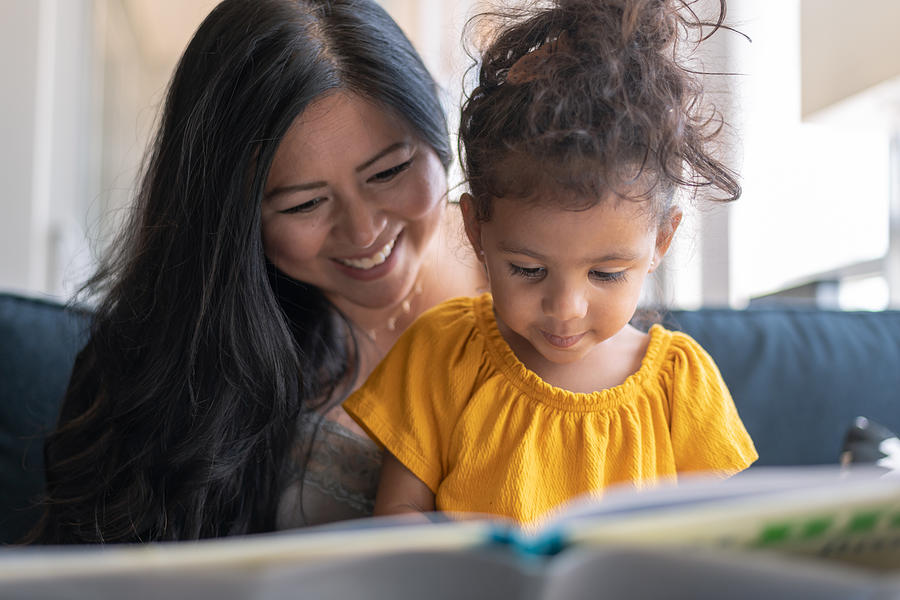 Adorable mixed race toddler reading book with her mother Photograph by Fly View Productions