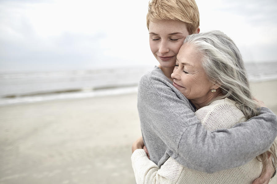 Adult daughter hugging senior mother on the beach Photograph by Oliver Rossi