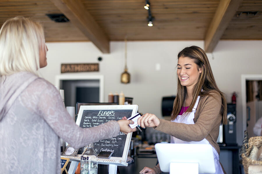 Adult female handing a barista a payment card Photograph by FatCamera