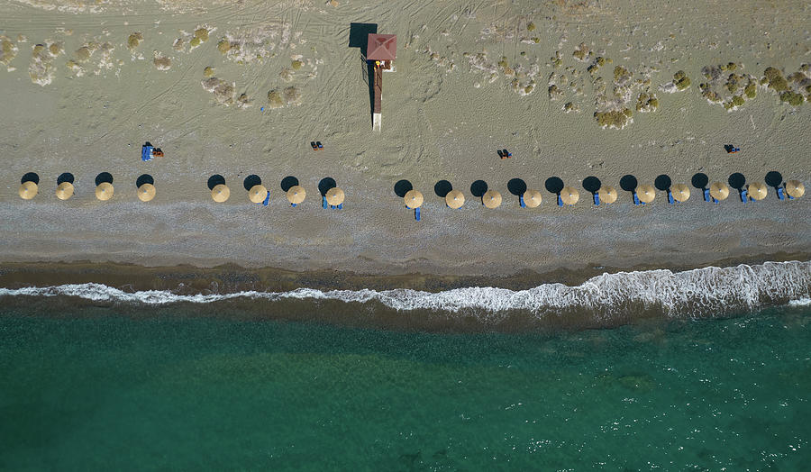 Aerial view from a flying drone of beach umbrellas in a row on an empty beach. Photograph by Michalakis Ppalis